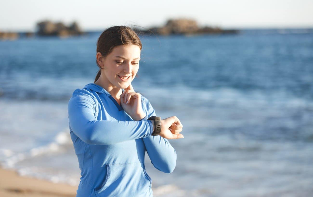 Woman running near ocean smiles and checks her running watch.