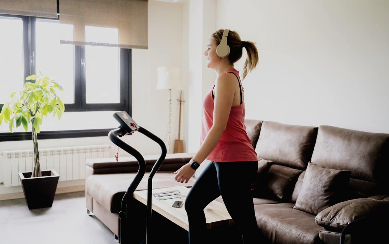 Woman listening to music and walking on a treadmill in her living room.