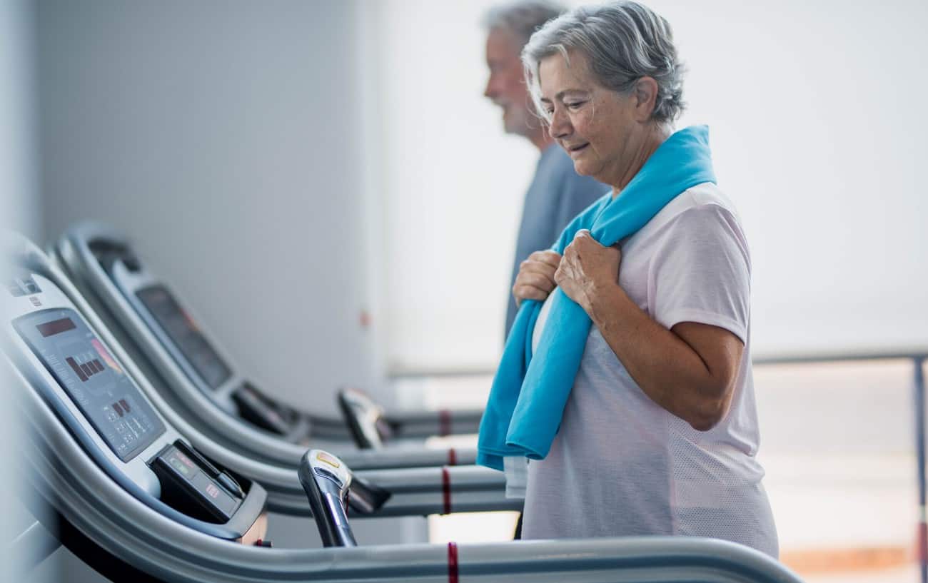 Senior woman with a blue town around her neck walking on a treadmill for seniors.