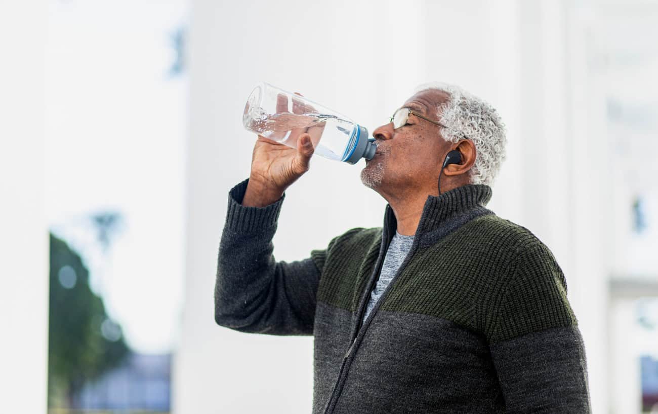 Senior man drinking water and listening to music after a workout.